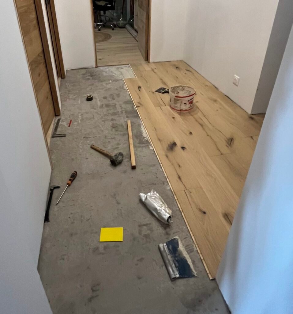 Artisan MyHomeRenov effectuant la pose collée d'un parquet massif